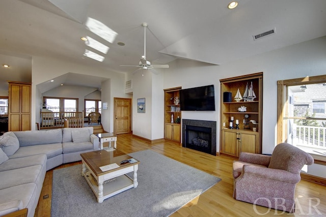 living room with light wood-type flooring, lofted ceiling, visible vents, and a tile fireplace