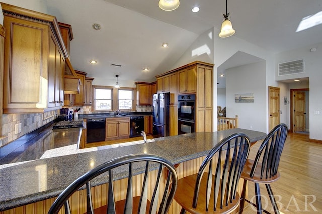 kitchen with visible vents, vaulted ceiling, hanging light fixtures, black appliances, and tasteful backsplash