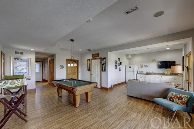 game room with light wood-style floors, visible vents, a textured ceiling, and baseboards