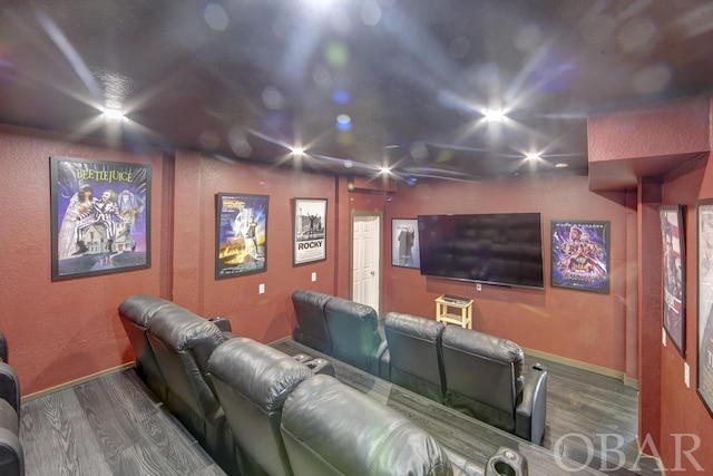 cinema room featuring a textured wall, baseboards, and wood finished floors