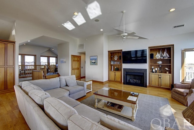 living room featuring vaulted ceiling, visible vents, a fireplace, and light wood-style flooring