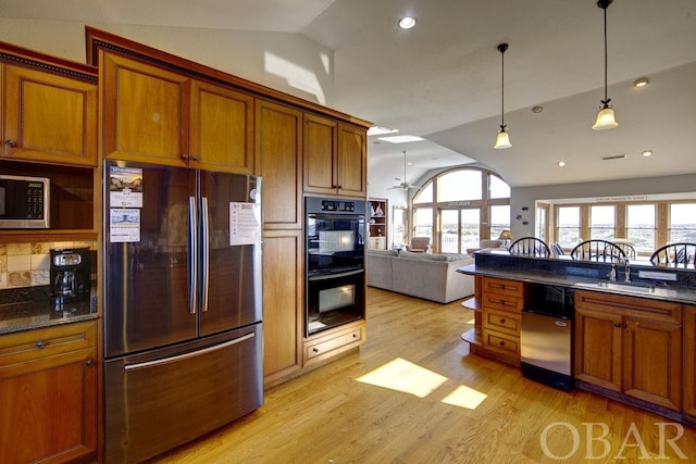 kitchen featuring light wood-style flooring, appliances with stainless steel finishes, open floor plan, hanging light fixtures, and vaulted ceiling