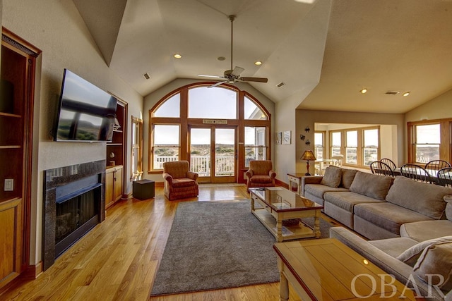 living area featuring built in features, lofted ceiling, a fireplace, and light wood-style flooring