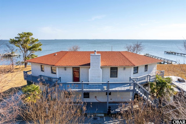 view of front of home featuring roof with shingles, stairway, a chimney, and a deck with water view