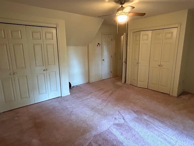 unfurnished bedroom featuring vaulted ceiling, carpet floors, two closets, and a ceiling fan