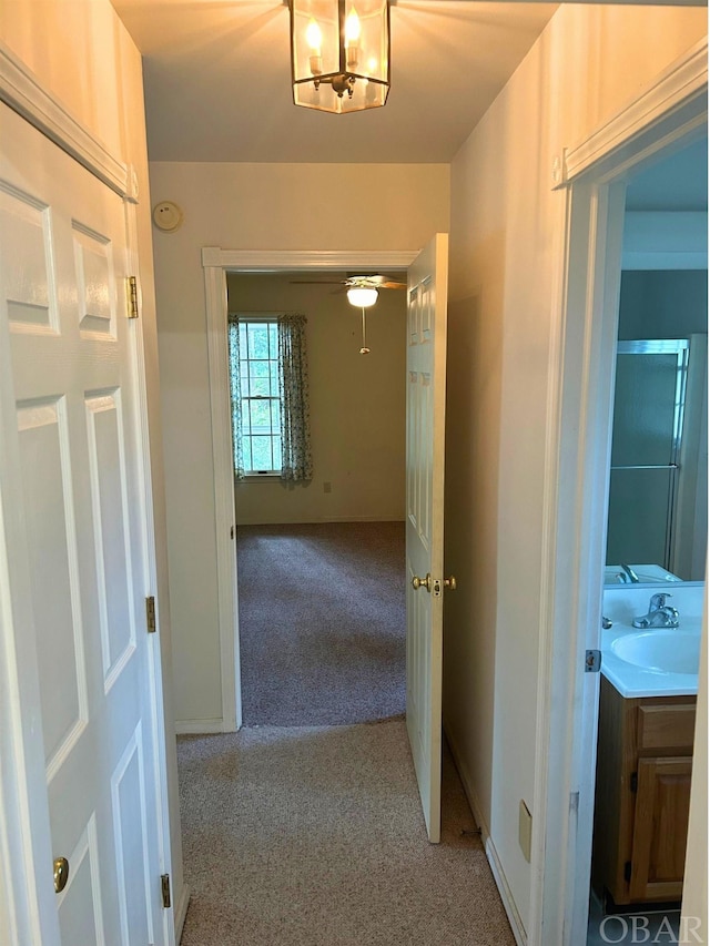 hallway featuring carpet, baseboards, and a sink