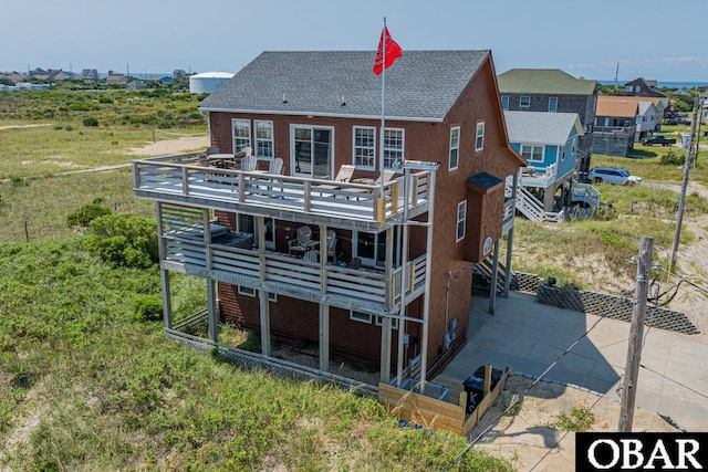 back of property with a deck, roof with shingles, and stairway