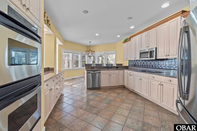 kitchen with backsplash, a peninsula, stainless steel appliances, pendant lighting, and a sink