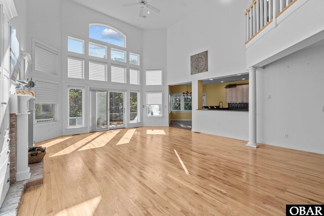 unfurnished living room with baseboards, a ceiling fan, a towering ceiling, light wood-style flooring, and ornate columns