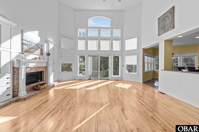 unfurnished living room featuring a wealth of natural light, a brick fireplace, a towering ceiling, and wood finished floors