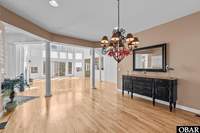 dining area featuring baseboards, an inviting chandelier, light wood-style flooring, and ornate columns