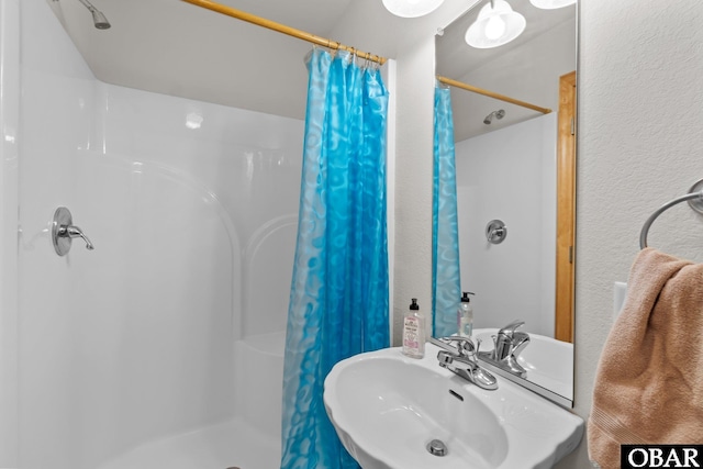 full bathroom featuring a shower with shower curtain, a textured wall, and a sink