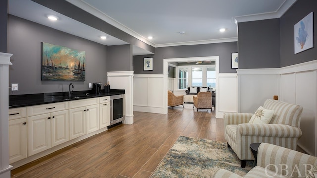 interior space featuring wine cooler, a sink, light wood-style floors, wainscoting, and indoor wet bar