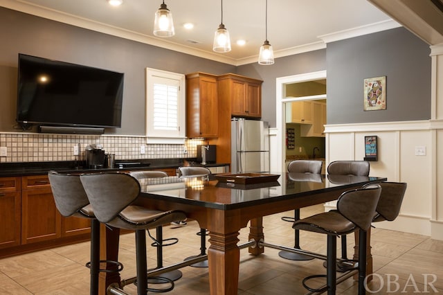 kitchen with decorative backsplash, dark countertops, a breakfast bar area, freestanding refrigerator, and hanging light fixtures