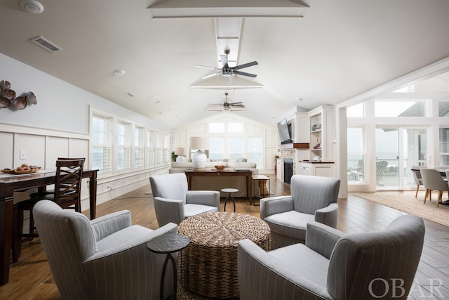 living room featuring visible vents, a decorative wall, a ceiling fan, vaulted ceiling, and wood finished floors