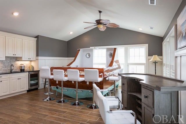 dining area with dark wood-style flooring, visible vents, vaulted ceiling, ceiling fan, and beverage cooler