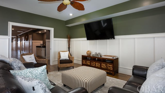 living area featuring ceiling fan, recessed lighting, a decorative wall, wood finished floors, and wainscoting