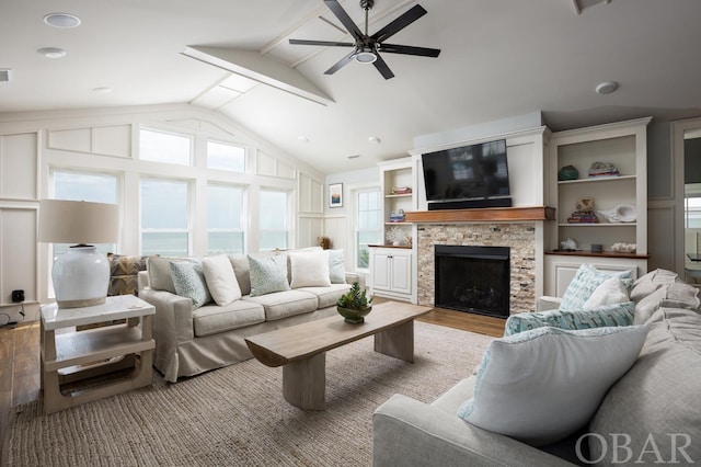 living room with a stone fireplace, light wood-style flooring, a decorative wall, a ceiling fan, and vaulted ceiling