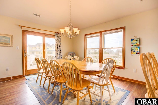 dining space featuring visible vents, a notable chandelier, baseboards, and wood finished floors