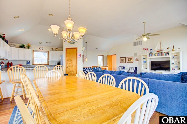 dining area with lofted ceiling, ceiling fan with notable chandelier, a fireplace, visible vents, and light wood-type flooring