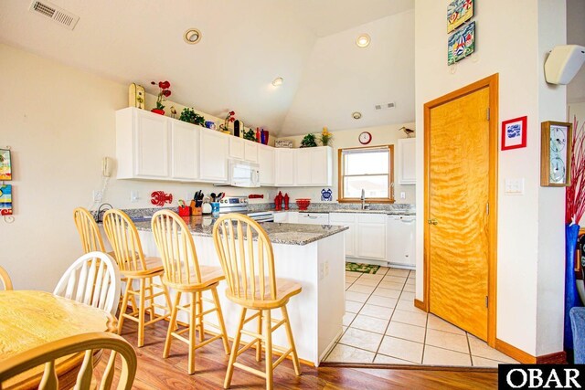 kitchen featuring a peninsula, white appliances, white cabinetry, and a breakfast bar