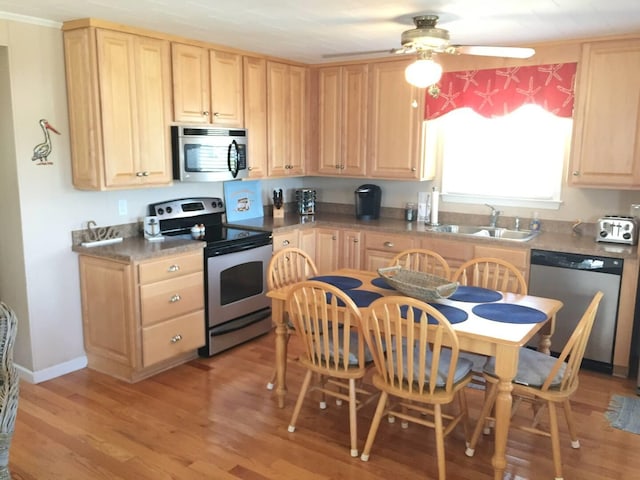 kitchen featuring light brown cabinets, stainless steel appliances, dark countertops, and a sink