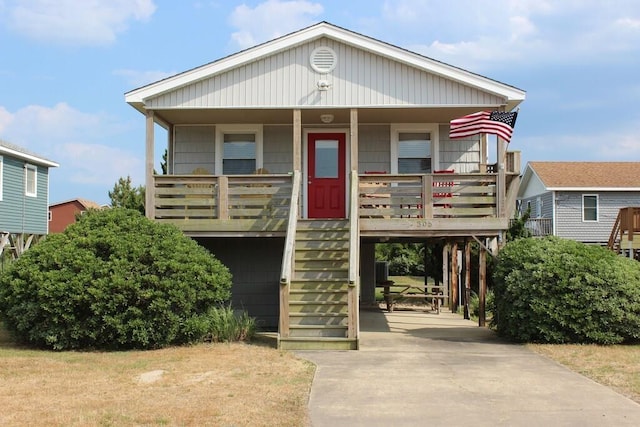 raised beach house featuring a carport, covered porch, stairway, and concrete driveway