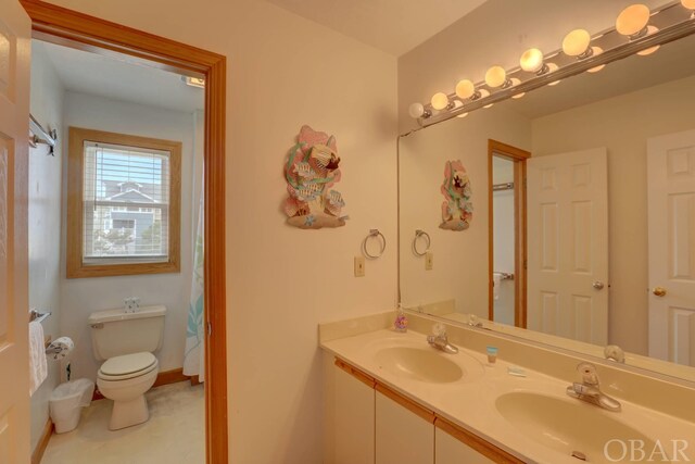 full bathroom with double vanity, a sink, toilet, and baseboards