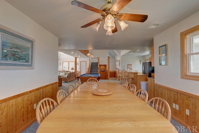 dining room featuring a wainscoted wall, wood walls, and stairs