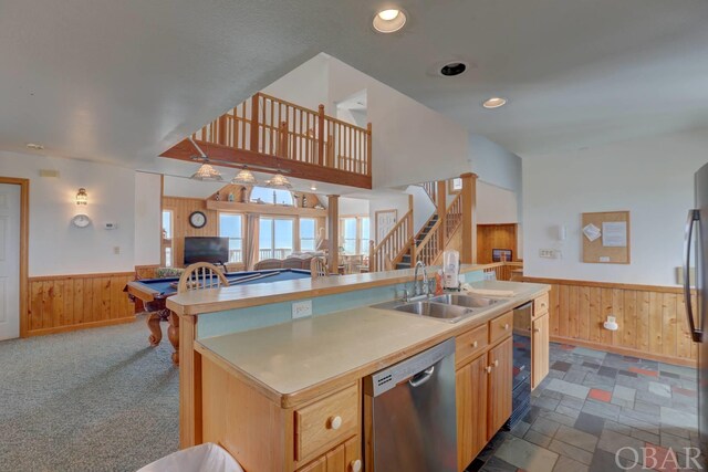 kitchen featuring wooden walls, a sink, open floor plan, appliances with stainless steel finishes, and wainscoting