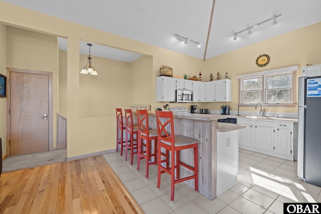 kitchen featuring white cabinets, stainless steel microwave, freestanding refrigerator, a kitchen bar, and a sink