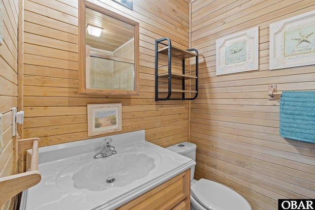 bathroom with a shower with shower door, wood walls, vanity, and toilet