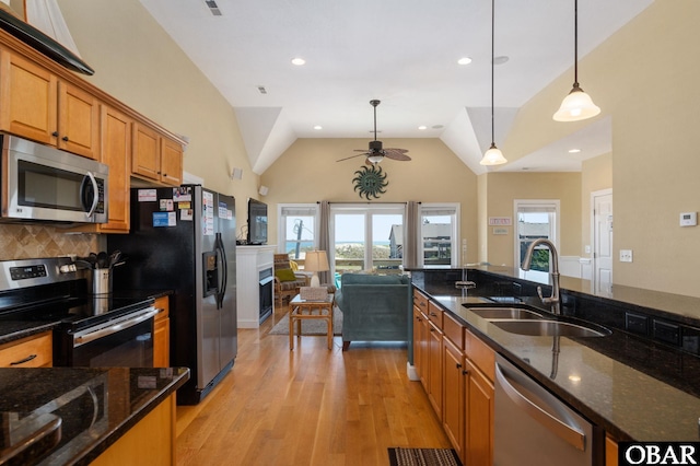 kitchen with light wood finished floors, a sink, brown cabinets, ceiling fan, and appliances with stainless steel finishes