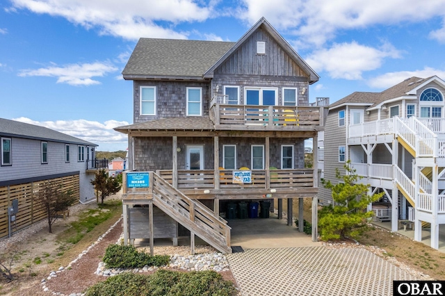 back of house with stairway, a shingled roof, a balcony, driveway, and a carport