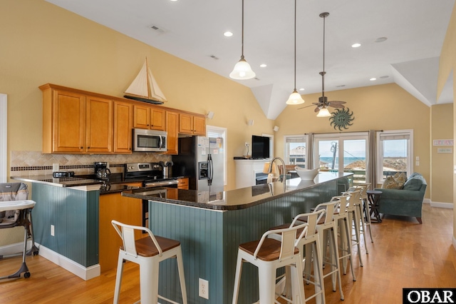 kitchen featuring light wood finished floors, tasteful backsplash, dark countertops, a ceiling fan, and appliances with stainless steel finishes