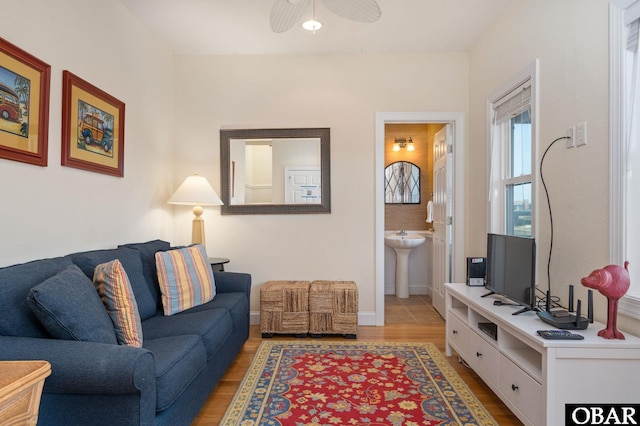 living area featuring light wood-style flooring, baseboards, and ceiling fan