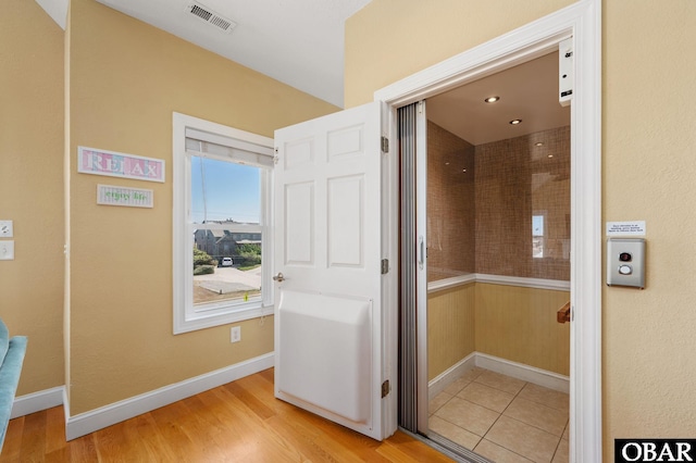 hallway featuring baseboards, light wood-style flooring, and visible vents
