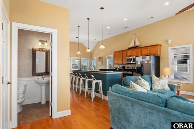 living area with light wood finished floors, a wainscoted wall, vaulted ceiling, baseboards, and visible vents