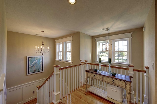 stairs featuring an inviting chandelier, visible vents, wood finished floors, and wainscoting