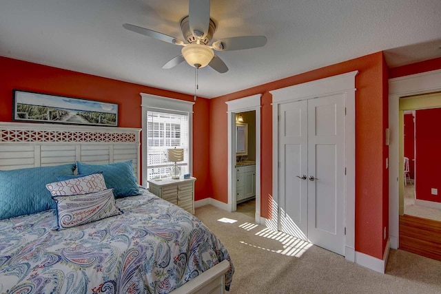 bedroom featuring baseboards, a ceiling fan, light colored carpet, ensuite bath, and a closet