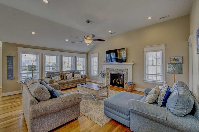 living area with lofted ceiling, a stone fireplace, light wood-style flooring, visible vents, and baseboards