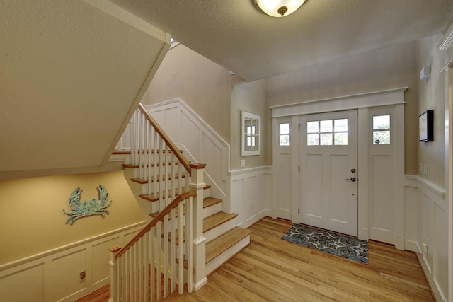 entryway featuring wainscoting, light wood-style flooring, stairs, a textured ceiling, and a decorative wall