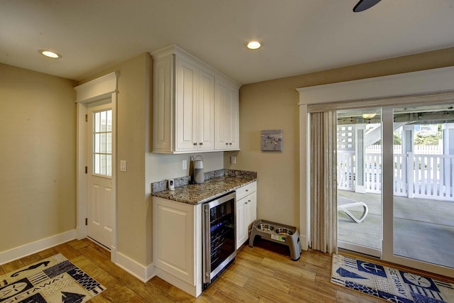 kitchen with a healthy amount of sunlight, beverage cooler, white cabinets, and dark stone countertops