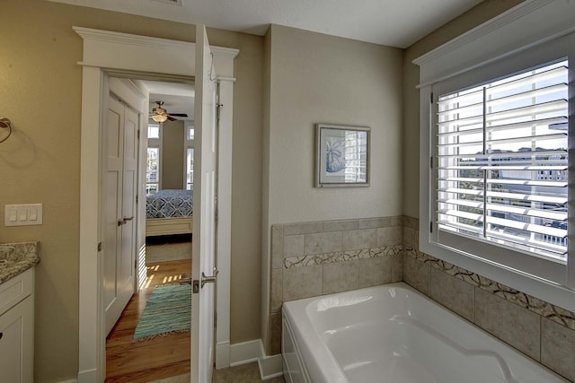 ensuite bathroom with baseboards, a ceiling fan, connected bathroom, a garden tub, and vanity