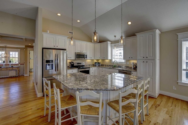 kitchen with appliances with stainless steel finishes, a center island, white cabinets, and light stone countertops