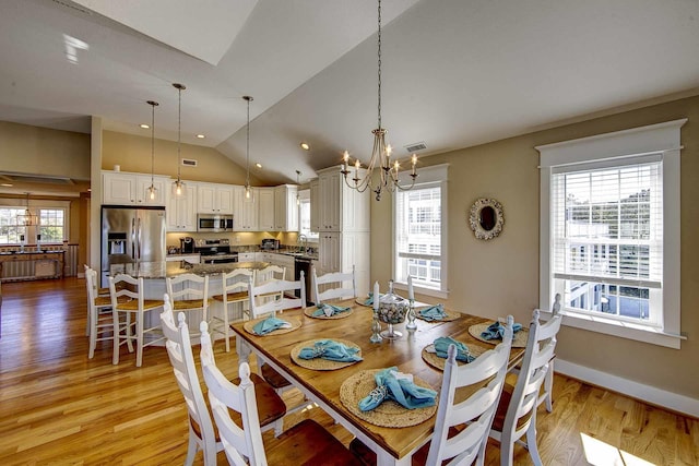 dining room featuring lofted ceiling, light wood finished floors, a wealth of natural light, and a notable chandelier