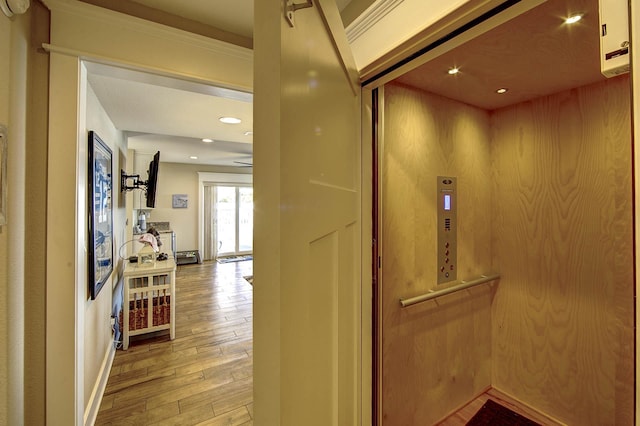 hallway featuring light wood finished floors, recessed lighting, and elevator