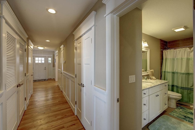 corridor with a wainscoted wall, light wood finished floors, a sink, and recessed lighting