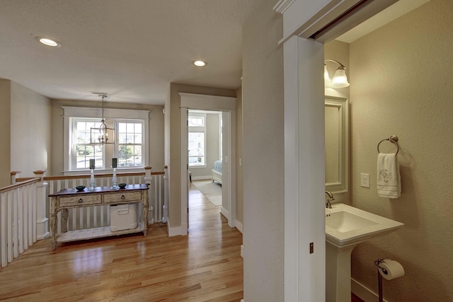 corridor with baseboards, recessed lighting, an inviting chandelier, and light wood-style floors