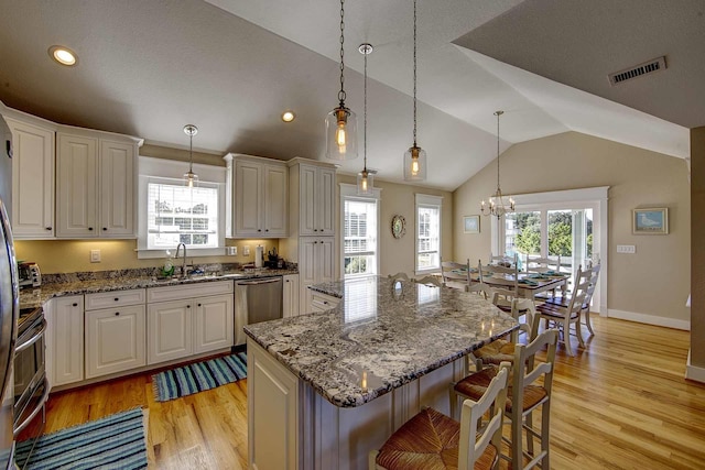 kitchen featuring visible vents, a kitchen island, hanging light fixtures, light stone countertops, and stainless steel appliances